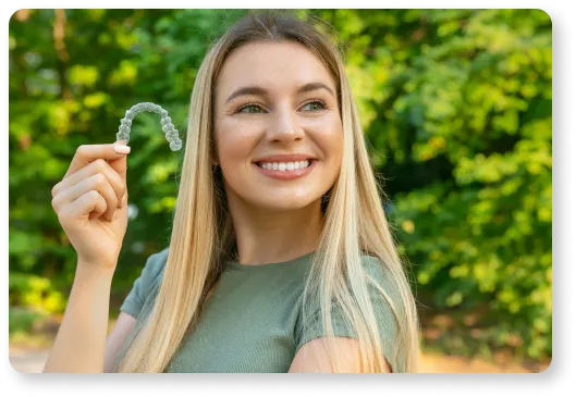 a woman holding up a clear aligner in front of her face